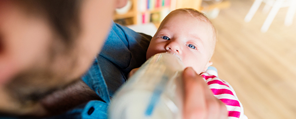 ein Mann hält ein Baby auf dem Arm und füttert es mit einer Flasche